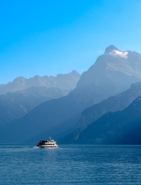 İsviçre Urnersee Gölü kıyısındaki dağların çizgileri - Luzerne Gölü - gündüz sisli ışıklarda. Göldeki turist gemisi.