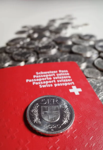 A five Swiss franc coin lies on a red Swiss passport