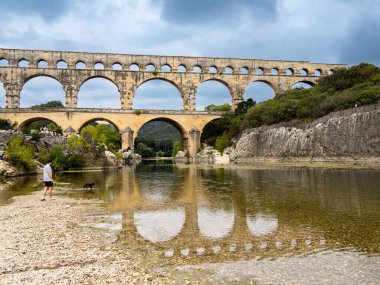 Pont du Gard, Fransa - 4 Ekim 2023: Bir adam köpeğini ünlü Roma Pont du Gard su kemeri altında gezdirir.