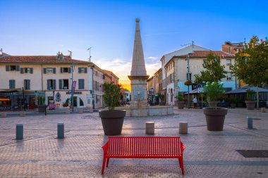 Saint Maximin, Fransa - 1 Ekim 2023 Saint Maximin la Sainte Baume meydanındaki kırmızı bank. Gün batımı zamanı.