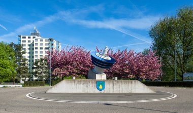 Birr, Switzerland - April 4, 2024: Industrial Alstom gas turbine as a decorative sculpture of roundabout and coat of arms of Birr clipart