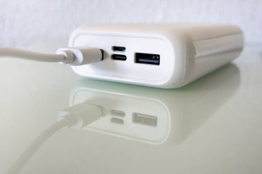 Beyaz güç bankası yansıtıcı cam zemin üzerinde bir USB kablosuna bağlı