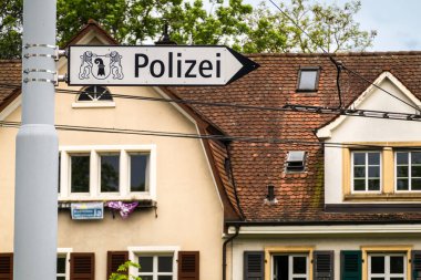Basel, İsviçre - 18 Mayıs 2024: Görüntü arkasında bir bina bulunan bir polis karakolunu işaret eden bir Alman sokak tabelasını gösteriyor.