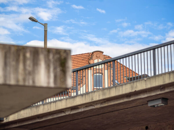 An urban scene featuring a concrete structure with a railing, a streetlamp, and a detailed building with a red tile roof.