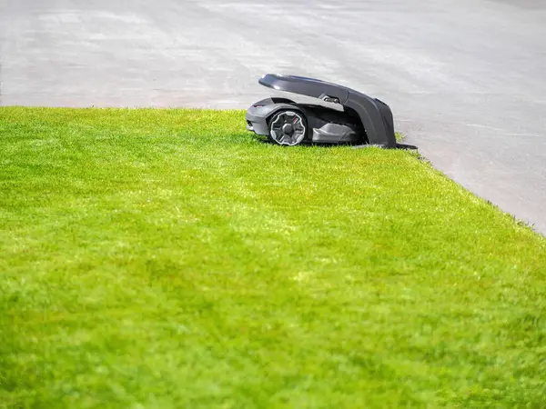 stock image A modern robotic lawn mower on grass and pavement, sleek design, lush green lawn, well-maintained, daytime scene.