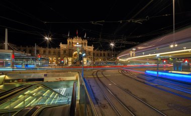 Zürih, İsviçre - 29 Mayıs 2024: Zürih 'te şehir gece sahnesi araç ışıkları, tarihi tren istasyonu binası, yeraltı girişi, yoğun tramvay rayları ve canlı şehir atmosferi.