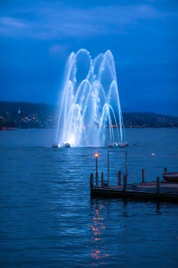 Serene lake Zurich view with illuminated water jet fountain at night. clipart