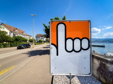 Mannedorf, Switzerland - June 13, 2024: Sunny street scene with hand traffic sign, cars, lake view. clipart