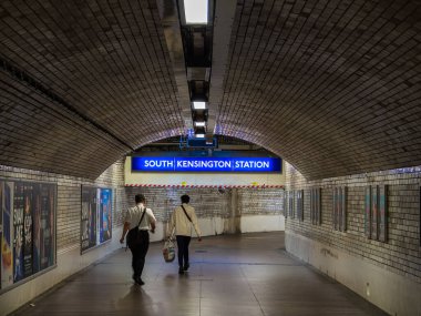 Londra, Birleşik Krallık - 25 Haziran 2024: Güney Kensington İstasyonu yeraltı tüneli beyaz ve kahverengi tuğlalar, floresan aydınlatma, posterler ve yürüyen iki kişi