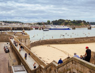 Saint Malo, Fransa - 20 Temmuz 2024: Saint Malo limanı ve marinası, insanlar kumlu plajın üzerindeki şehir duvarları boyunca yürüyorlar