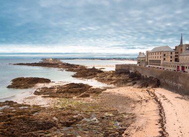 Saint Malo, Fransa - 20 Temmuz 2024: Sarp kayalıkları, kumlu plajı, bulutlu gökyüzü ve küçük adaları olan Saint Malo kıyıları.