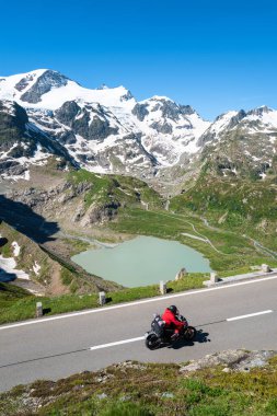 Sustenpass, İsviçre - 5 Temmuz 2024: Kırmızı ceketli maceraperest bisikletçi dağ yoluna çıkıyor. Steingletcher buzulu ve Steinsee gölü Sustenpass dağ geçidinde..
