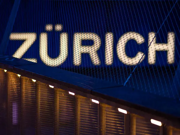 stock image A bright illuminated ZURICH sign at night near a railway station, blue hour and warm lights in the foreground.