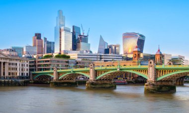 Londra, Birleşik Krallık - 25 Haziran 2024: Thames nehri boyunca modern gökdelenlerin yer aldığı canlı bir şehir, günbatımının sıcaklığını yansıtıyor.