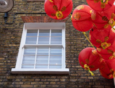 London, United Kingdom - June 25, 2024: A white-framed window on a brick wall with red Chinese lanterns hanging nearby - China town in London clipart