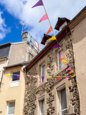 Renkli bayraklarla süslenmiş sokak sahnesi. Binalar taştan yapılmış ve canlı yüzleri var.,