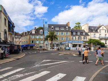 Biniç, Fransa - 21 Temmuz 2024: Biniç Meydanı 'nda tarihi binalar ve belirgin mavi işareti olan bir otelle çevrili yayalar karşıdan karşıya geçiyor.