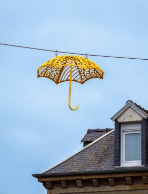 A vibrant yellow decorative umbrella hanging from a wire against a clear blue sky. The umbrella features a unique design, adding an artistic touch to the scene. clipart