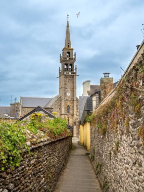 Bulutlu bir gökyüzünün altında eski taş duvarlar ve binalarla çevrili tarihi bir kiliseye giden dar bir taş yol. Conquet Köyü, Brittany