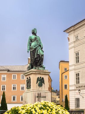 Salzburg, Avusturya - 24 Ekim 2024: Memleketi Salzburg 'da büyüleyici binaları ve çiçekleri olan Bronz Mozart heykeli.