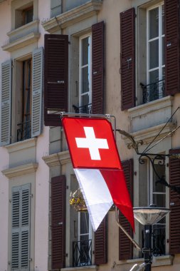 Morges 'in dış binasında kırmızı ve beyaz bir İsviçre bayrağı sallanıyor. Pencerelerde koyu kahverengi panjurlar var. Binanın klasik bir Avrupa mimari tarzı var..
