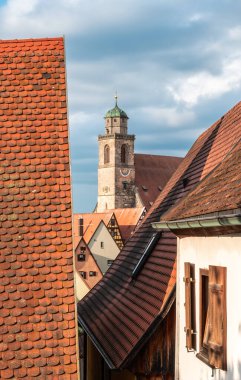 Avrupa 'nın tarihi Dinkelsbuhl kasabasının manzarası. Kırmızı kiremitli çatıları ve bulutlu gökyüzünün altında önemli bir kilise kulesi var..