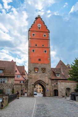 Dinkelsbuhl, Almanya - 7 Ağustos 2024: Şehir kapısı ve Dinkelsbuhl 'daki tarihi kule, renkli binalar. Çakıl taşı kaldırımları kuleye doğru gidiyor. Arabalar yan tarafa park edilmiş..