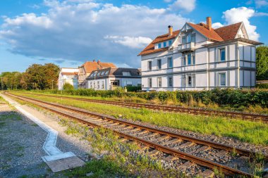 A scenic view of a railway track running alongside residential houses in Bad Mergentheim under a blue sky with clouds. clipart