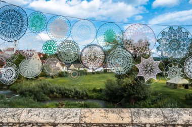 Yeşil tarlalardan oluşan bir arkaplanda asılı renkli dantel örtüler ve bulutlu mavi bir gökyüzü. Altlıklar doğal manzarayla çok güzel bir kontrast oluşturuyor..