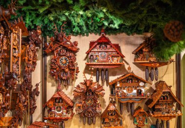 Rothenburg ob der Tauber, Almanya - 8 Ağustos 2024: Duvarda sergilenen, çeşitli stil ve dekorasyonların yer aldığı, yeşil yapraklarla çevrili, karmaşık bir şekilde tasarlanmış ahşap guguklu saat koleksiyonu.