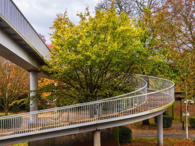 Londra 'da yeşil ağaçlarla çevrili beyaz korkulukları olan eğimli yaya köprüsü..