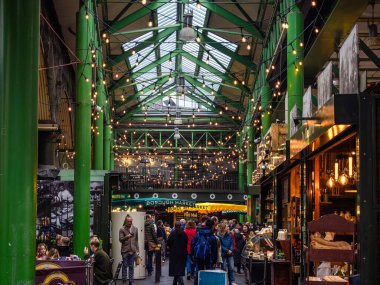 Londra, Birleşik Krallık - 27 Ekim 2024: Yeşil sütunları, tel lambaları ve çeşitli tezgahları olan hareketli bir Borough pazarı. İnsanlar alışveriş yapıyor ve etrafta dolanıyor..