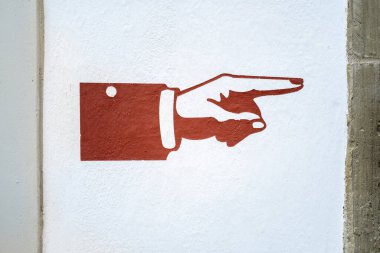 Sağı gösteren kırmızımsı-kahverengi bir el beyaz bir duvara boyanmıştır. Basit tasarım net bir yön göstergesi olarak hizmet eder. Duvar dokusu görünür..