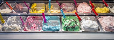 Metal kaplarda çeşitli renkli gelato tatları sergilenir. Dondurma kremalı ve lezzetli görünüyor, servis edilmeye hazır..