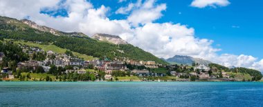 İsviçre 'de Sankt Moritz' in pitoresk bir kasabası ve parlak mavi gökyüzünün altında yemyeşil dağlarla çevrili bir göl. Güzel bir yaz günü sahnesi.