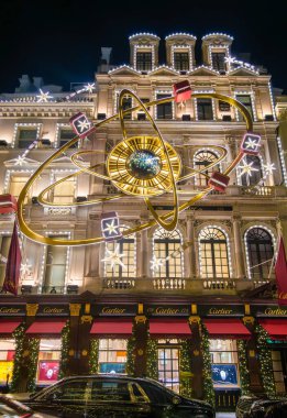 Londra, Birleşik Krallık - 25 Kasım 2024: Büyük bir altın saat, şenlik ışıkları ve bayram süslemelerinin yer aldığı gece Cartier binası ve mağazası güzel bir Noel süslemesi,