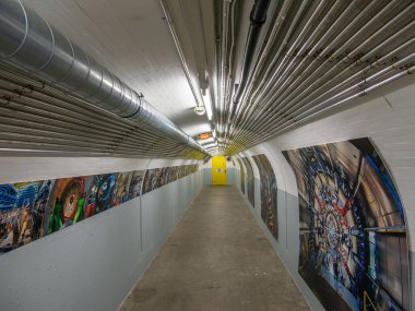 Cenevre, İsviçre - 5 Şubat 2025: CERN, ATLAS yeraltı sanayi koridoru, canlı bilimsel duvar resimleri ve parlak sarı bir kapı.