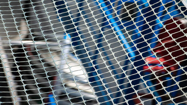 Крупный план металлической сетки с размытым абстрактным промышленным фоном.