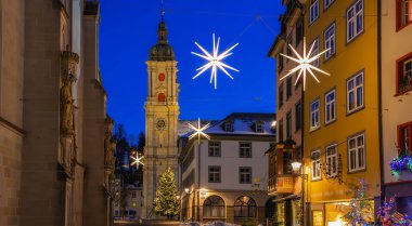 Sankt Gallen, İsviçre - 1 Ocak 2025: St. Gallus katedralinin çan kulesi, geceleri aydınlatma. Parlak yıldız şekilli ışıklar ve Noel ağacı şenlikli bir atmosfer yaratır..