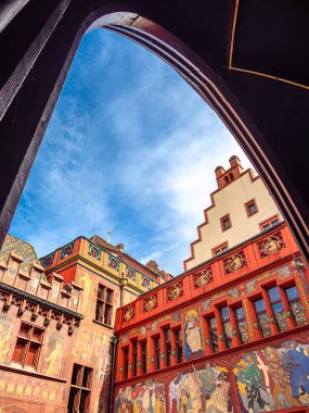 Basel, İsviçre - 17 Ağustos 2024: Tarihi bir belediye binası olan Basel 'in canlı bir mimari sahnesi, süslü fresklerle süslenmiş ve mavi gökyüzüne karşı bir kemer deliğinden bakılan bir basamak..