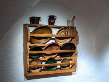 Michaelbeuern, Avusturya - 22 Ekim 2024: Beyaz bir duvara karşı renkli kırsal seramik kaseler ve sürahiler sergilenen ahşap bir raf. Antika yemekler..