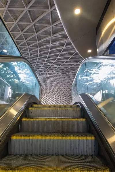 Londra, Birleşik Krallık - 13 Kasım 2024: Geniş, mimari açıdan çarpıcı bir binaya çıkan modern bir yürüyen merdiven. Tavanda parlak, havadar bir atmosferi olan geometrik bir tasarım var..
