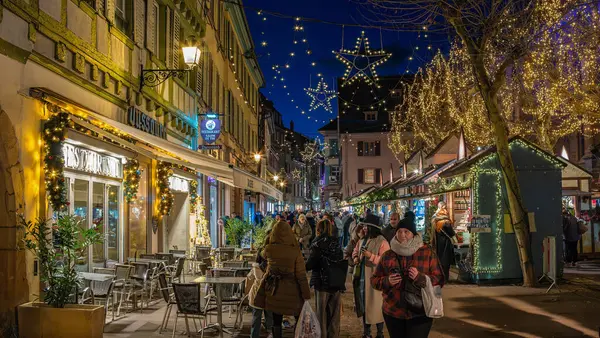 Colmar, Fransa - 28 Kasım 2024: Bayram döneminde Colmar 'da sokak sahnesi, festival dekorasyonları, aydınlık binalar ve atmosferin keyfini çıkaran bir grup insan.