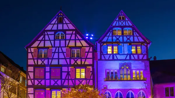 Colmar, Fransa - 28 Kasım 2024: Colmar 'da geceleri pencereleri aydınlatılmış iki geleneksel yarı keresteli ev, klasik Alsas mimarisi sergileniyor.