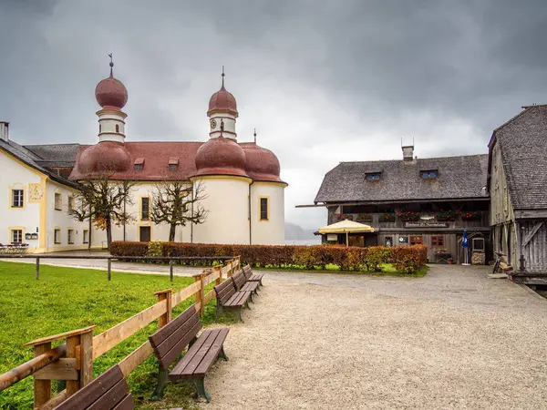 Schonau, Almanya - 23 Ekim 2024: Bulutlu bir günde deniz kenarında bulunan kendine özgü kırmızı soğan kubbeleriyle St. Bartholoma Kilisesi manzarası. Ahşap iskele ve yeşil tabela.