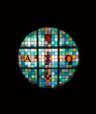 Michaelbeuern, Avusturya - 22 Ekim 2024: Renkli geometrik desenlere ve Alfa ve Omega harflerine sahip dairesel bir vitray.