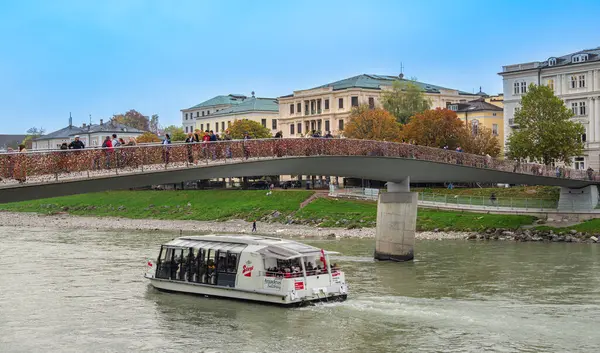 Salzburg, Avusturya - 24 Ekim 2024: Salzburg 'da Marko Feingold Steg köprüsü altında aşk kilitleriyle süslenmiş modern bir nehir teknesi seyahat ediyor