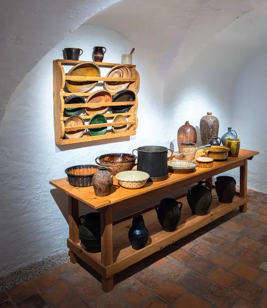 Michaelbeuern, Avusturya - 22 Ekim 2024: Ahşap raflarda çeşitli seramik ve metal kaplar, sürahiler ve kâselerin sergilendiği bir kırsal mutfak sahnesi.