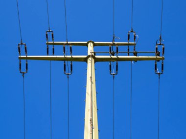 Mavi gökyüzüne karşı yüksek voltajlı iletim hatları olan elektrik direği.