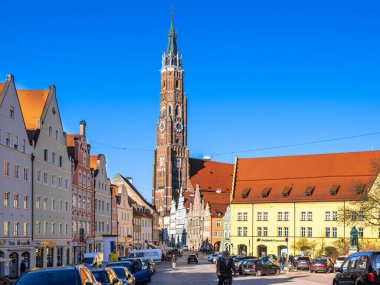 Landshut, Almanya - 19 Mart 2025: Renkli binalar ve açık mavi gökyüzüyle çevrili uzun bir saat kulesinin yer aldığı tarihi Landshut şehir meydanı manzarası.